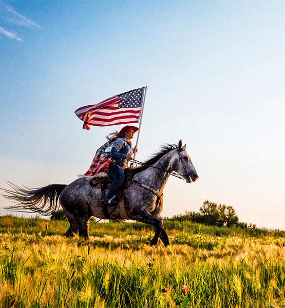 Cowboy on horseback carrying the American flag across a field